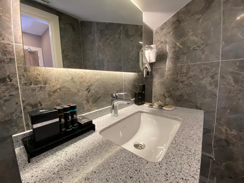 Un lavabo et des produits de toilette sur un comptoir clair dans une salle de bain carrelée.
