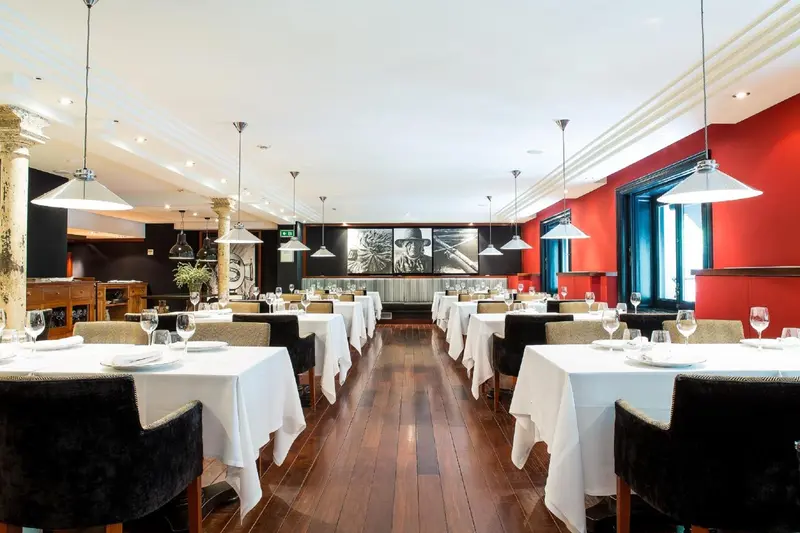 Une salle de restaurant lumineuse avec des tables nappées et des suspensions.