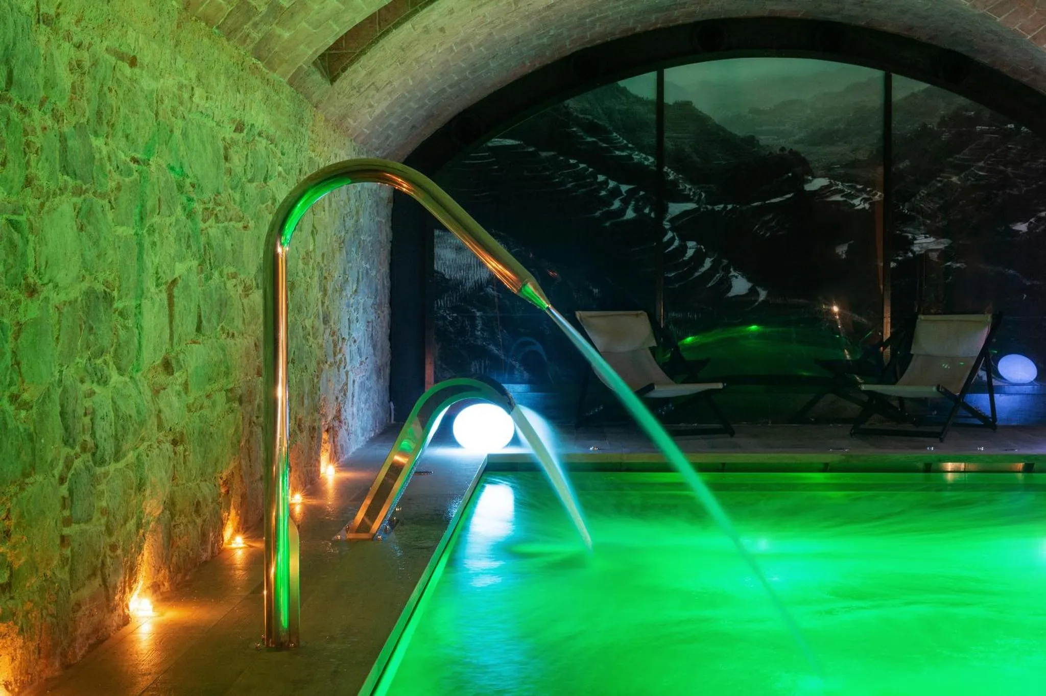 Une piscine intérieure illuminée en vert avec des transats à proximité.