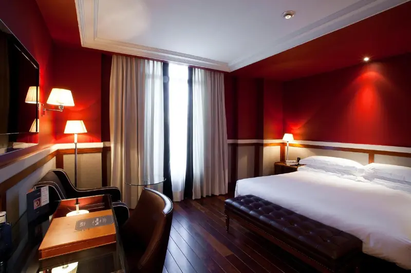 Une chambre avec un lit blanc et un bureau noir, aux murs rouge et blanc.