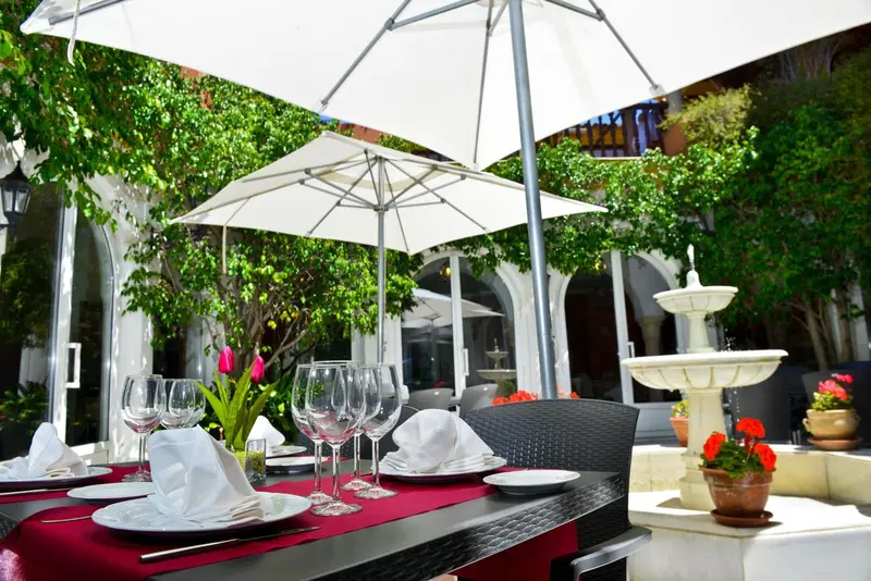 Une table dressée sur une terrasse ombragée avec une fontaine en arrière-plan.