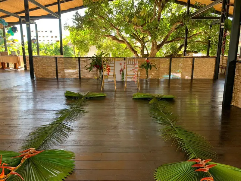Une allée décorée de feuillages mène à un espace ouvert ombragé par des arbres.
