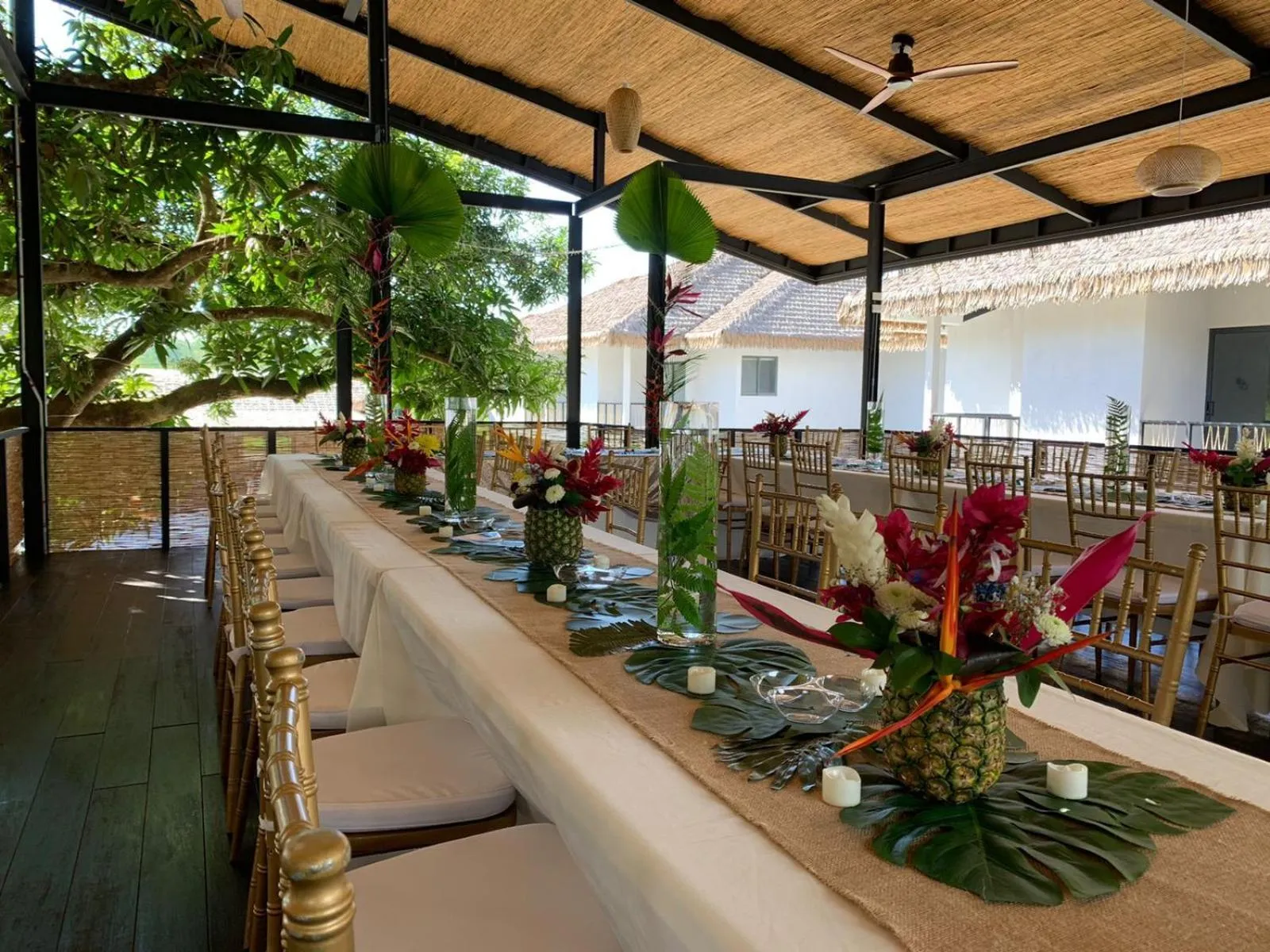 Une longue table dressée pour un repas en extérieur, décorée de fleurs tropicales et de bougies.