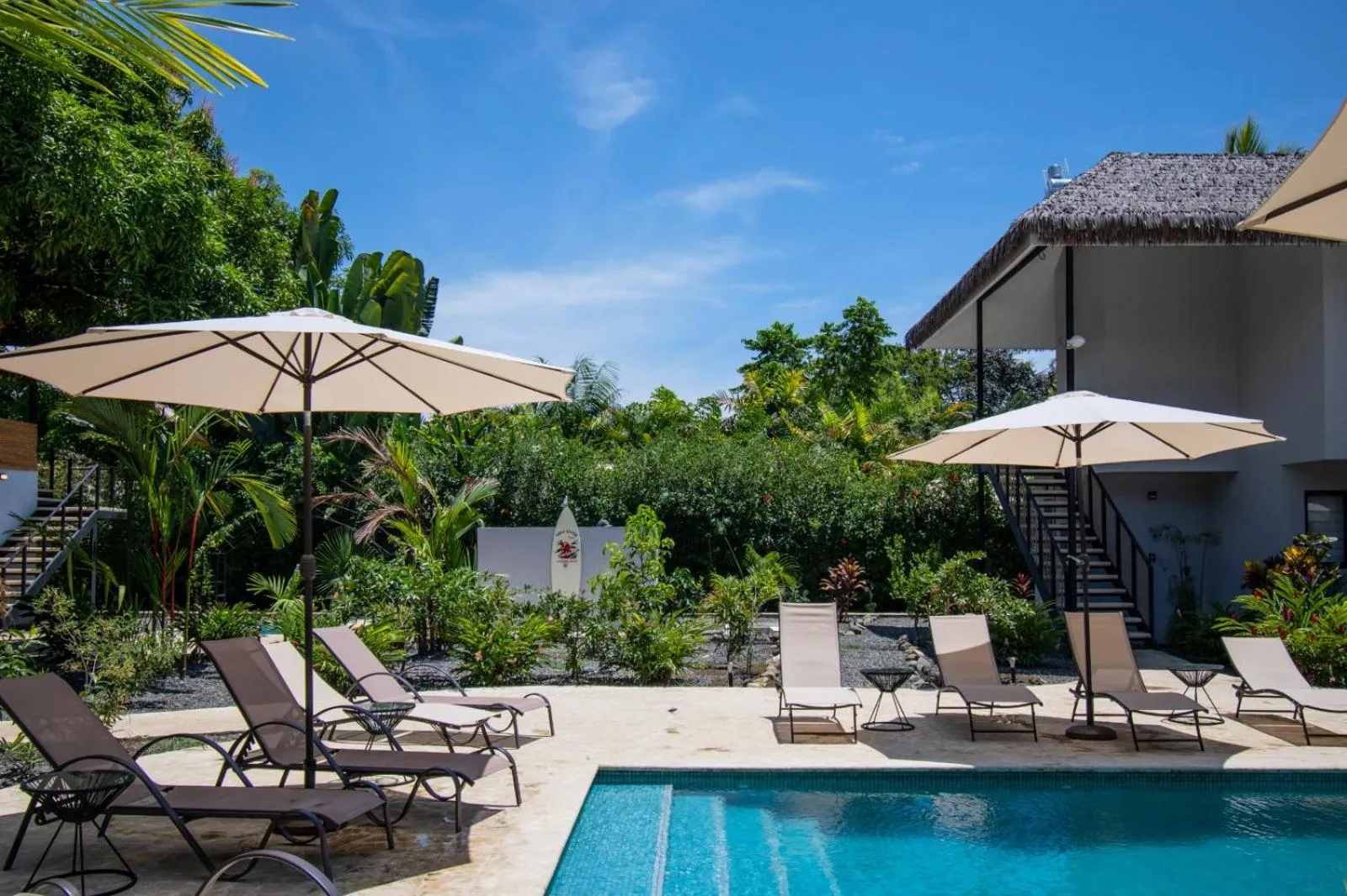 Transats et parasols ombragent une piscine dans un jardin tropical.