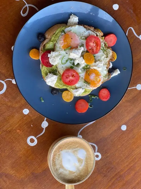 Assiette de pain grillé garni d'avocat, d'oeufs et de tomates, accompagnée d'une boisson chaude.