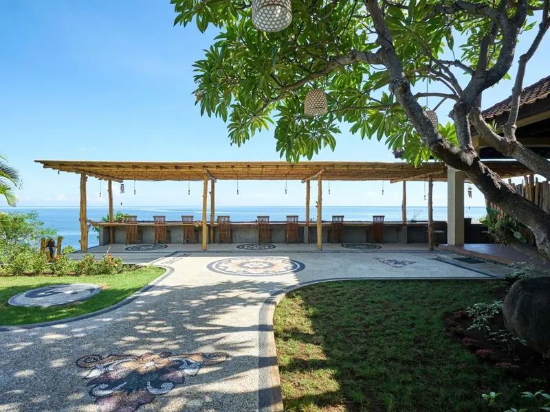 Terrasse ombragée avec bar donnant sur l'océan et un jardin soigné.