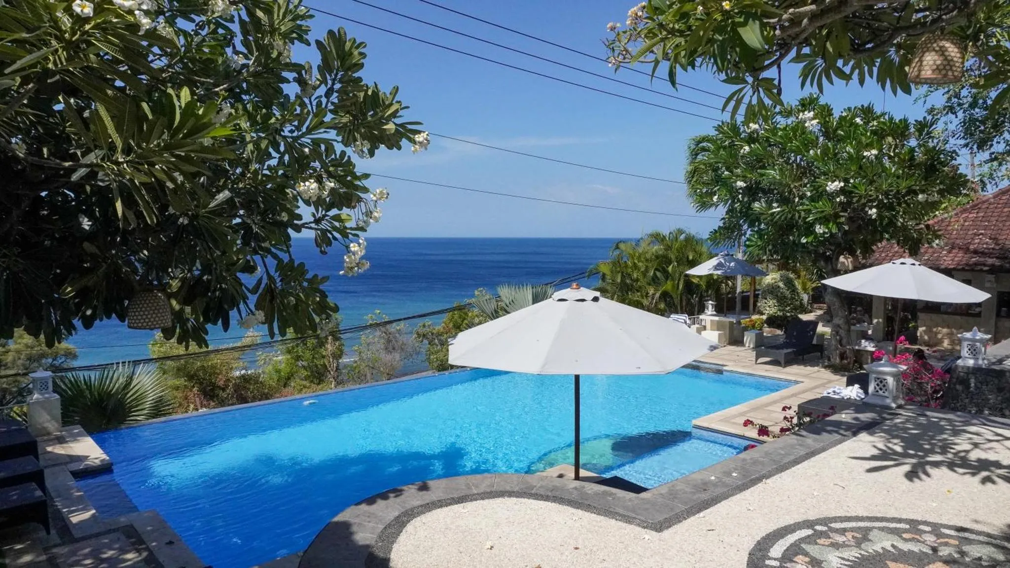 Une piscine turquoise bordée d'une terrasse ensoleillée avec vue sur la mer.