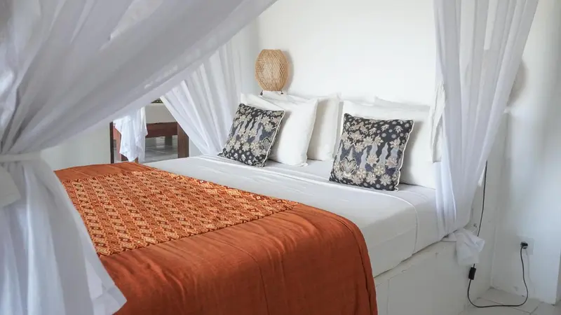 Un lit recouvert de moustiquaire et de coussins dans une chambre lumineuse.