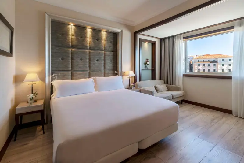 Une chambre lumineuse avec un grand lit et un coin salon près de la fenêtre.
