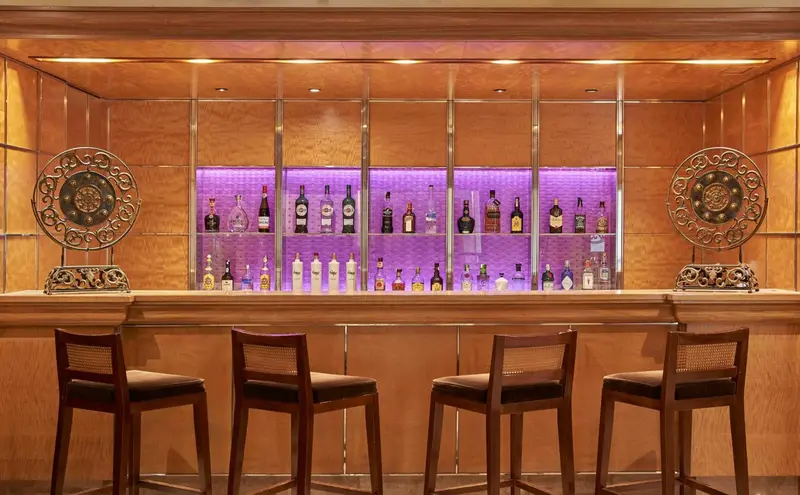 Un comptoir de bar en bois avec des tabourets et des bouteilles illuminées.