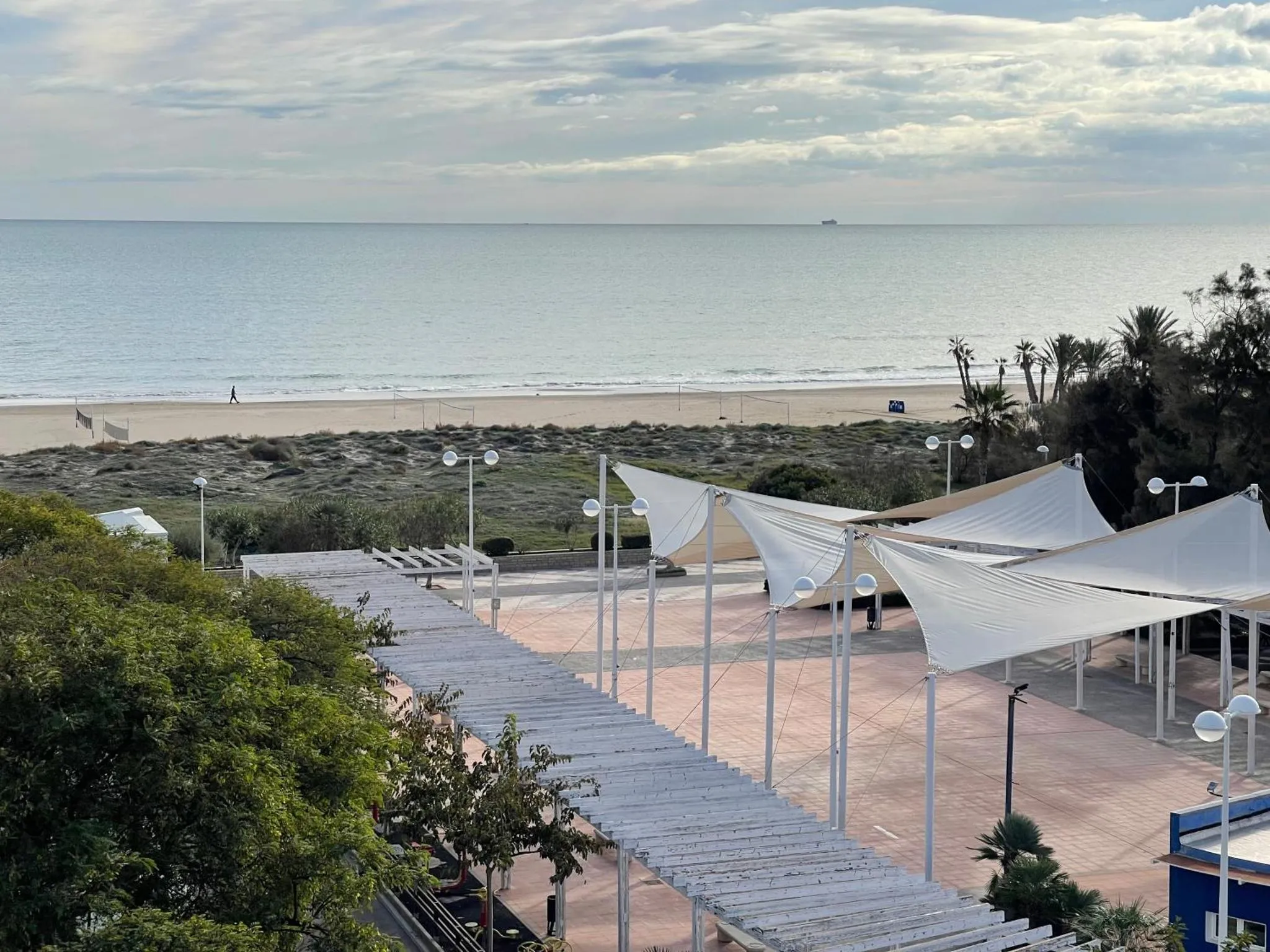 Terrasse ombragée surplombant une plage de sable fin et la mer.