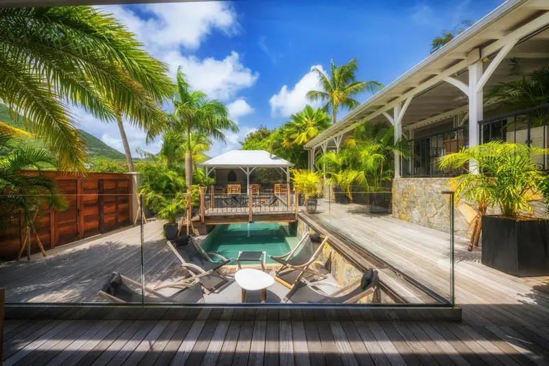 Terrasse en bois avec piscine et végétation luxuriante.