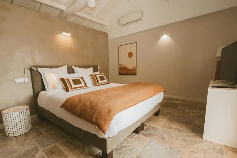 Une chambre lumineuse avec un grand lit recouvert d'une courtepointe orange et de coussins décoratifs.