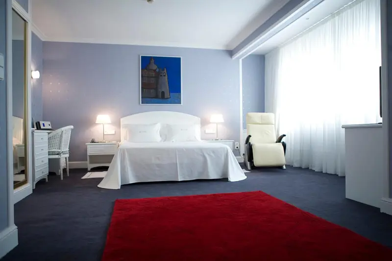 Chambre lumineuse avec un grand lit blanc et un fauteuil relax.