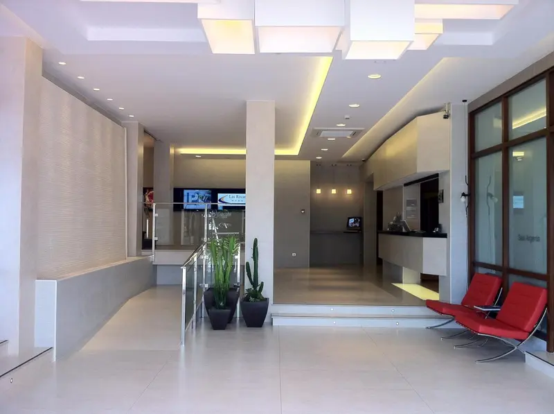 Hall d'entrée lumineux avec comptoir d'accueil et assises rouges.