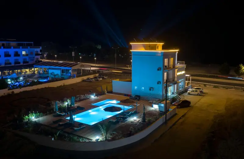 Vue nocturne d'un bâtiment illuminé avec une piscine et un parking.