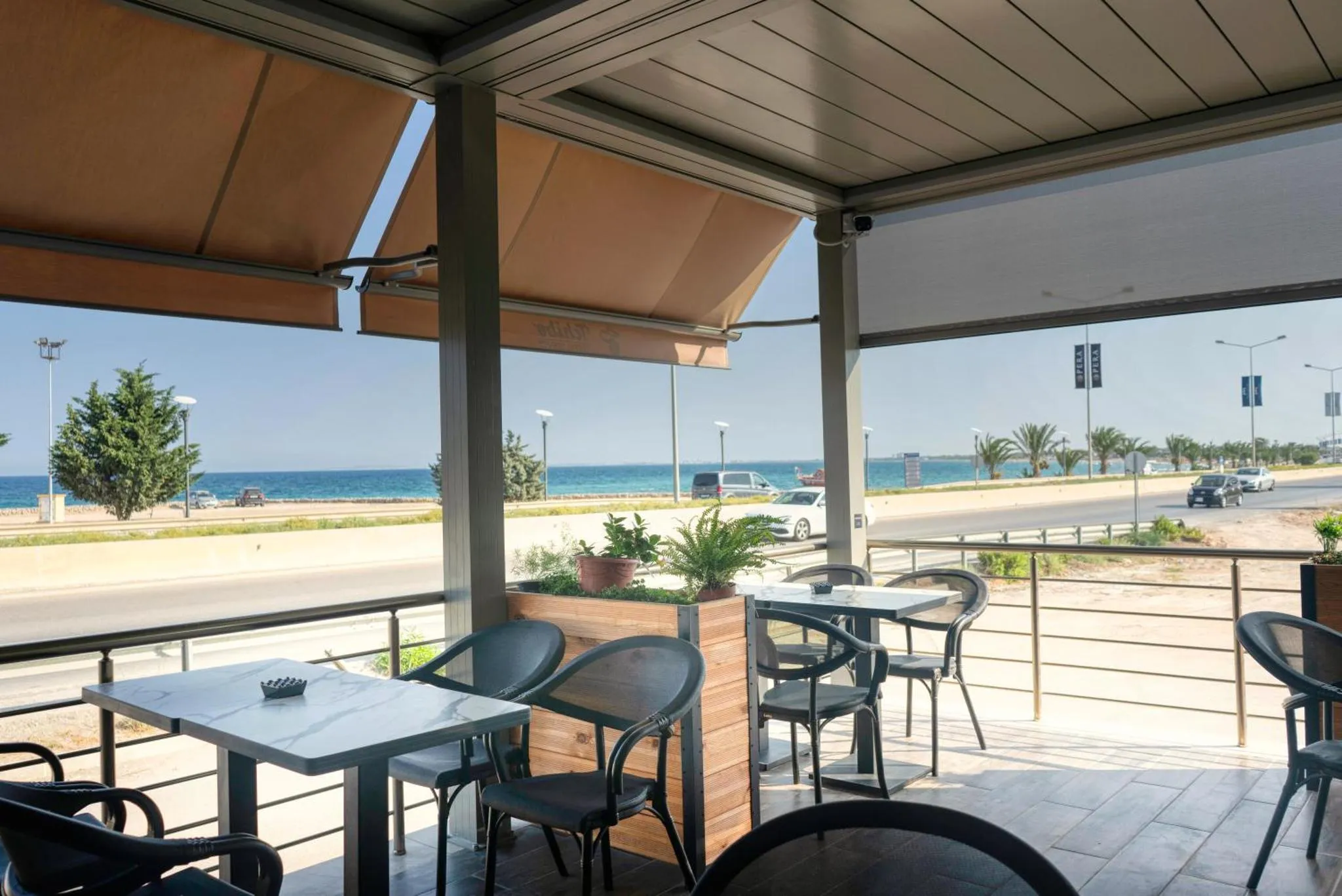 Terrasse ombragée avec tables et chaises donnant sur la mer.