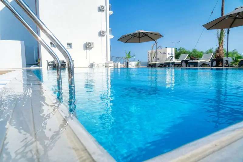 Une piscine bleu clair avec des transats et des parasols à proximité d'un bâtiment blanc.