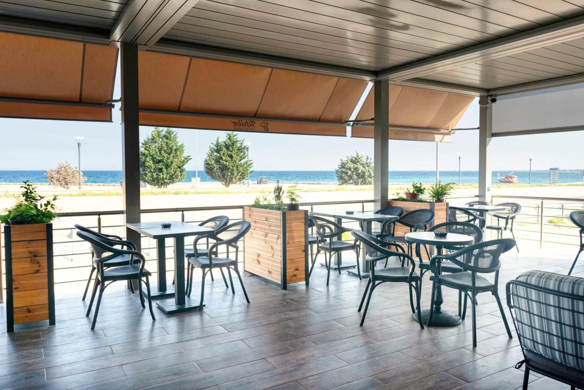 Terrasse ombragée avec tables et chaises donnant sur la mer.