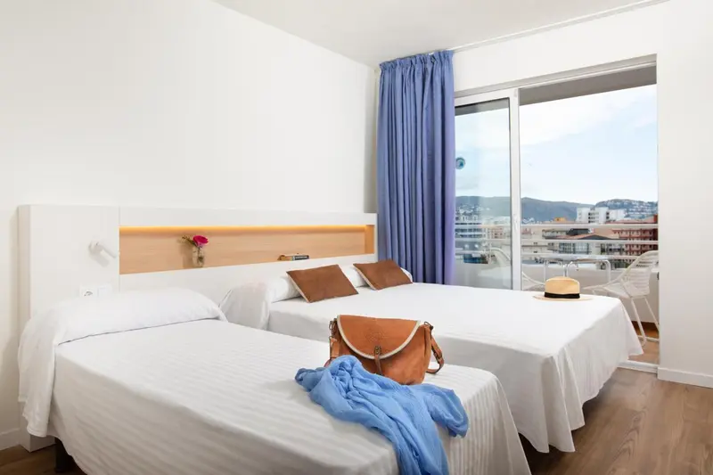 Une chambre lumineuse avec un lit double et un lit simple, donnant sur une vue urbaine.