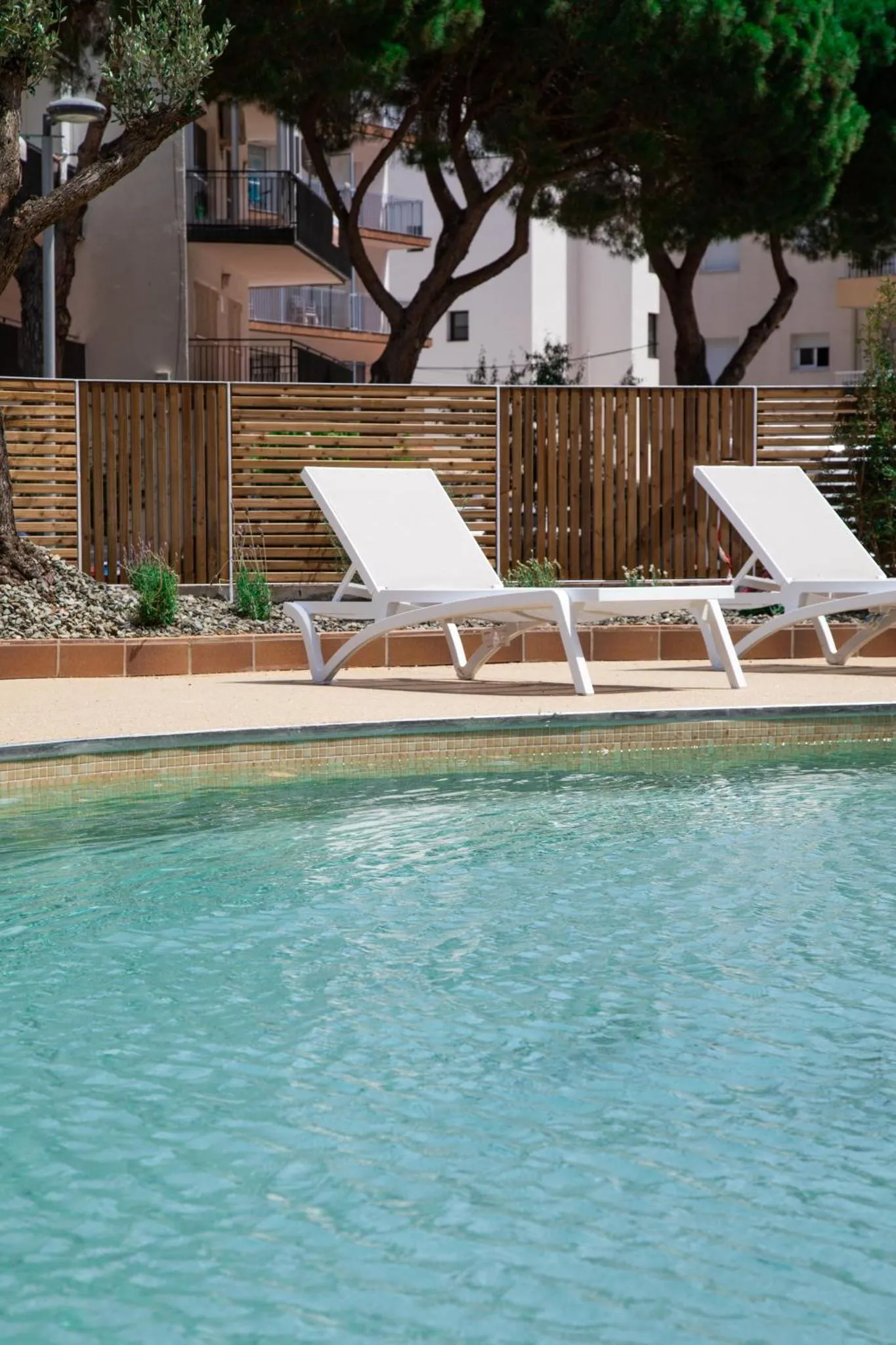 Deux transats blancs sont posés au bord d'une piscine turquoise.