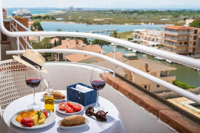 Une table ronde avec des verres de vin et des assiettes de nourriture sur un balcon ensoleillé.