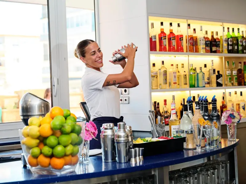 Une barmaid prépare un cocktail devant un comptoir bien garni.