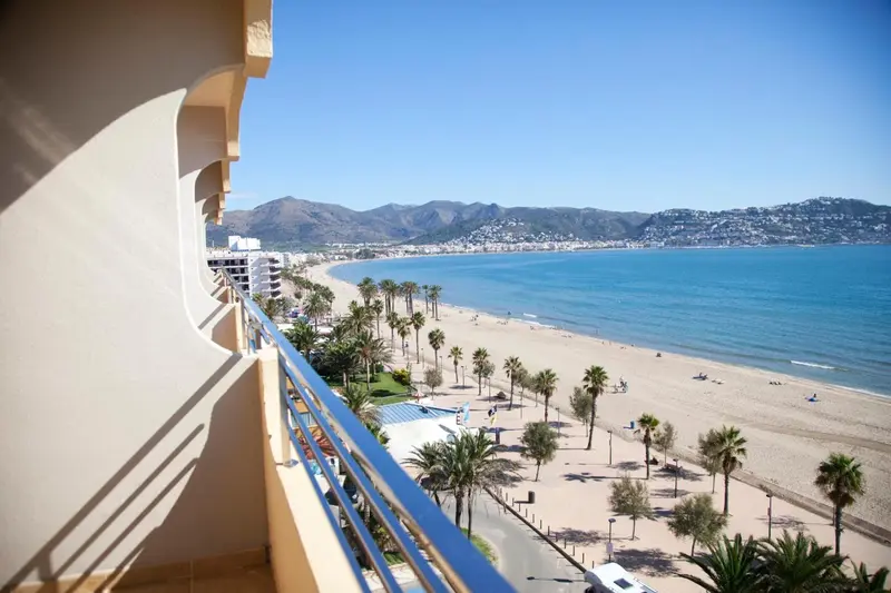 Vue d'une terrasse sur une plage de sable fin et une mer bleue.