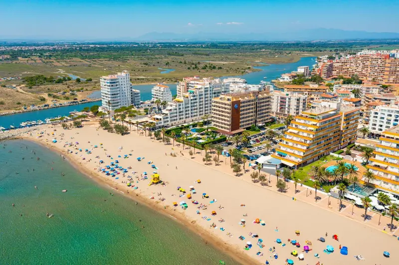 Vue aérienne d'une station balnéaire avec une longue plage de sable fin et des bâtiments blancs.