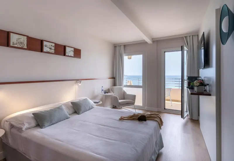 Chambre lumineuse avec un grand lit et une vue sur la mer depuis un balcon.