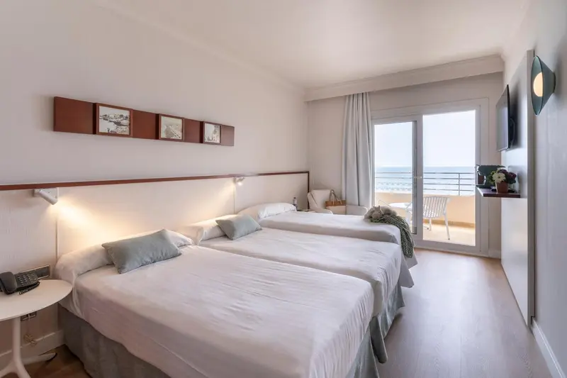 Chambre lumineuse avec deux lits simples et balcon donnant sur la mer.