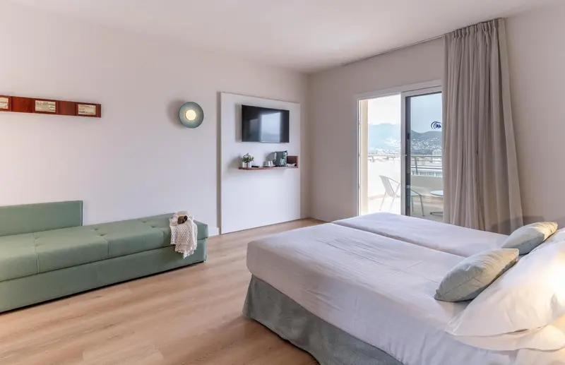 Une chambre lumineuse avec un canapé et un lit double donnant sur une vue dégagée.