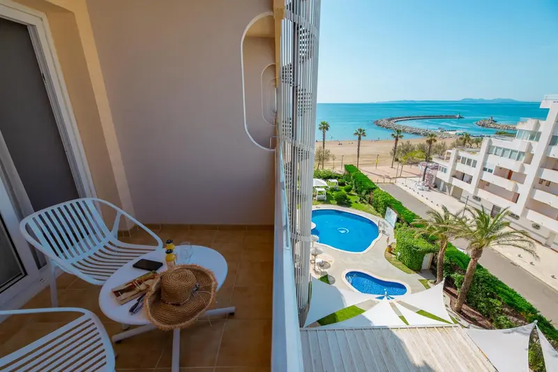 Balcon avec mobilier blanc donnant sur une piscine et la mer.