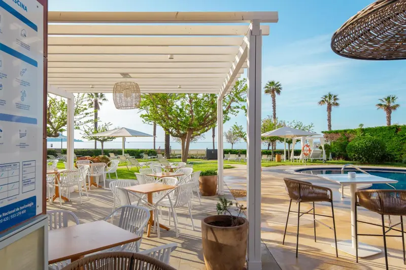 Terrasse ombragée avec tables et chaises donnant sur une pelouse et la mer.