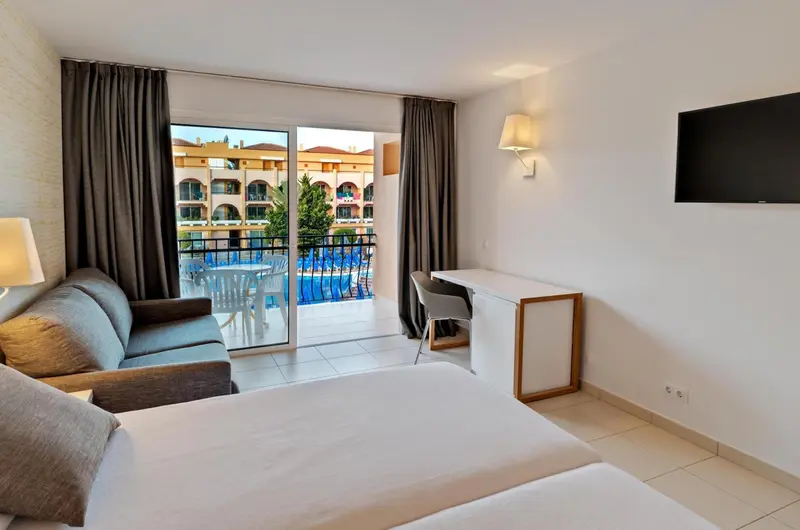 Une chambre lumineuse avec un canapé et un bureau donnant sur une piscine.