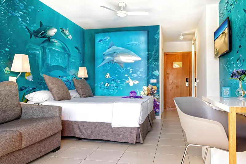 Une chambre lumineuse avec un lit double et un canapé face à un mur décoré de motifs marins.