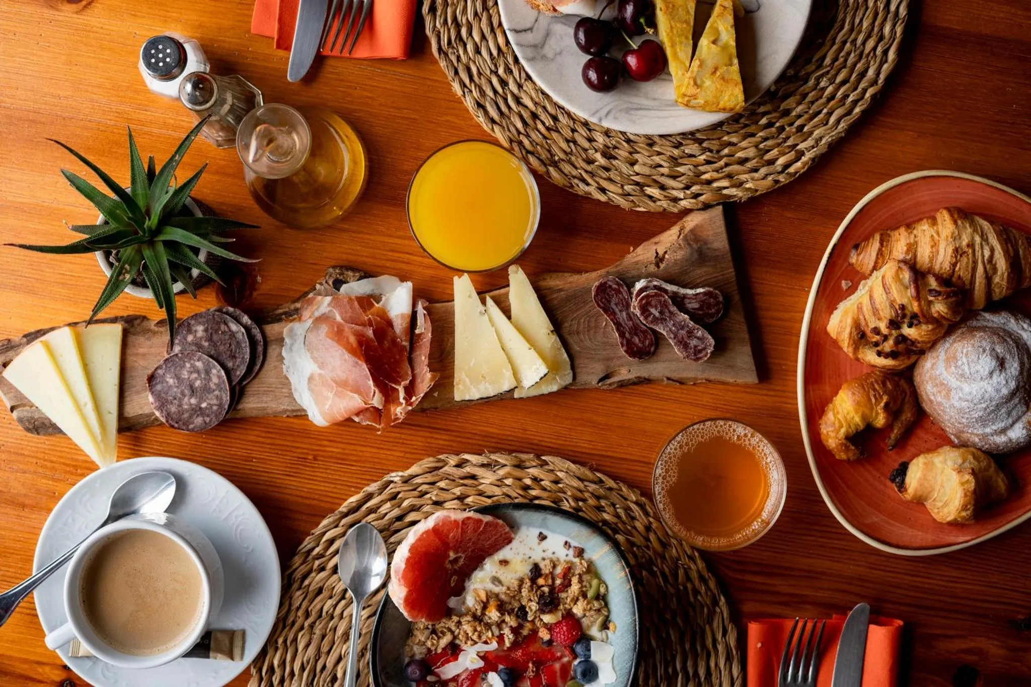 Table dressée avec un petit-déjeuner copieux composé de viennoiseries, de charcuterie, de fromages et de fruits.