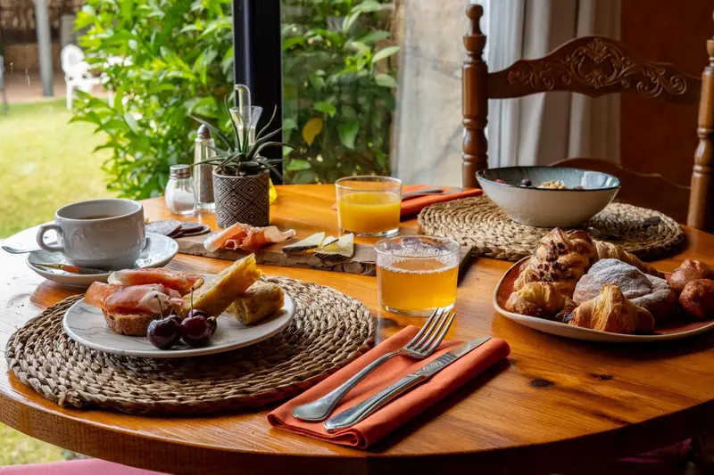 Une table ronde en bois est dressée pour un petit-déjeuner avec des viennoiseries et des fruits.