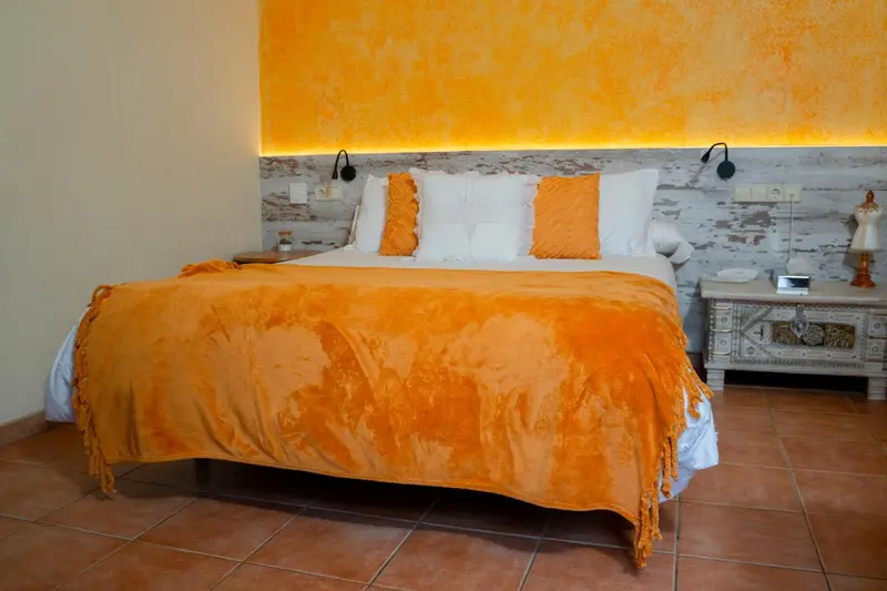 Une chambre lumineuse avec un grand lit recouvert d'une couverture orange.