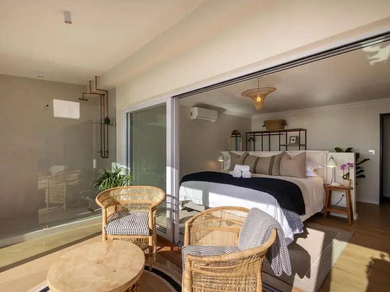 Une chambre lumineuse s'ouvre sur une terrasse avec des fauteuils en rotin.