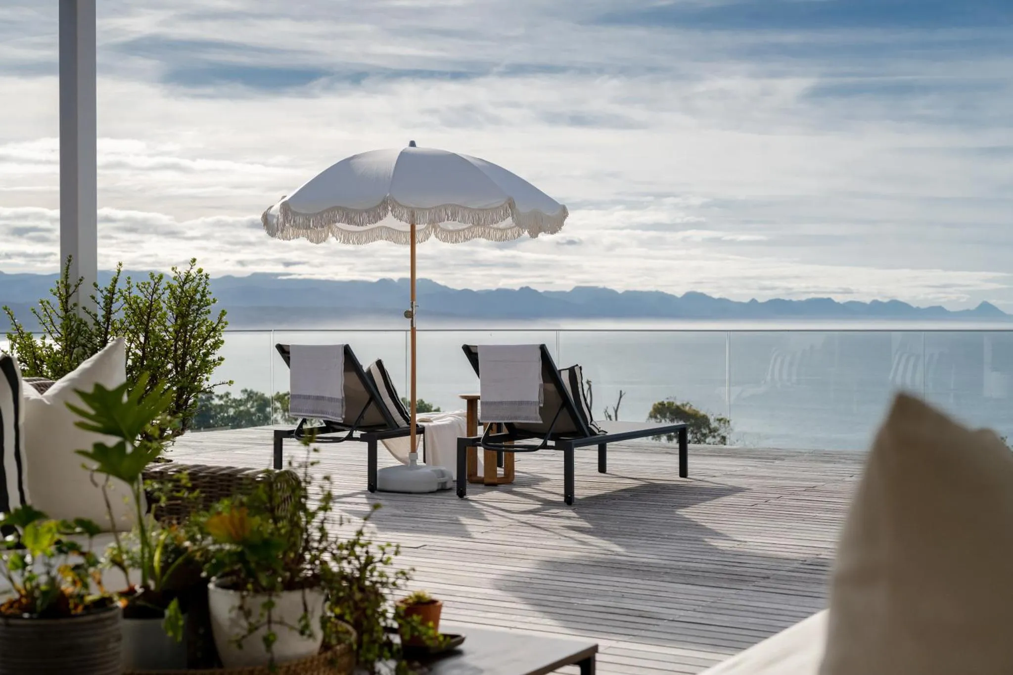 Deux chaises longues blanches invitent à la détente sur une terrasse en bois face à la mer.