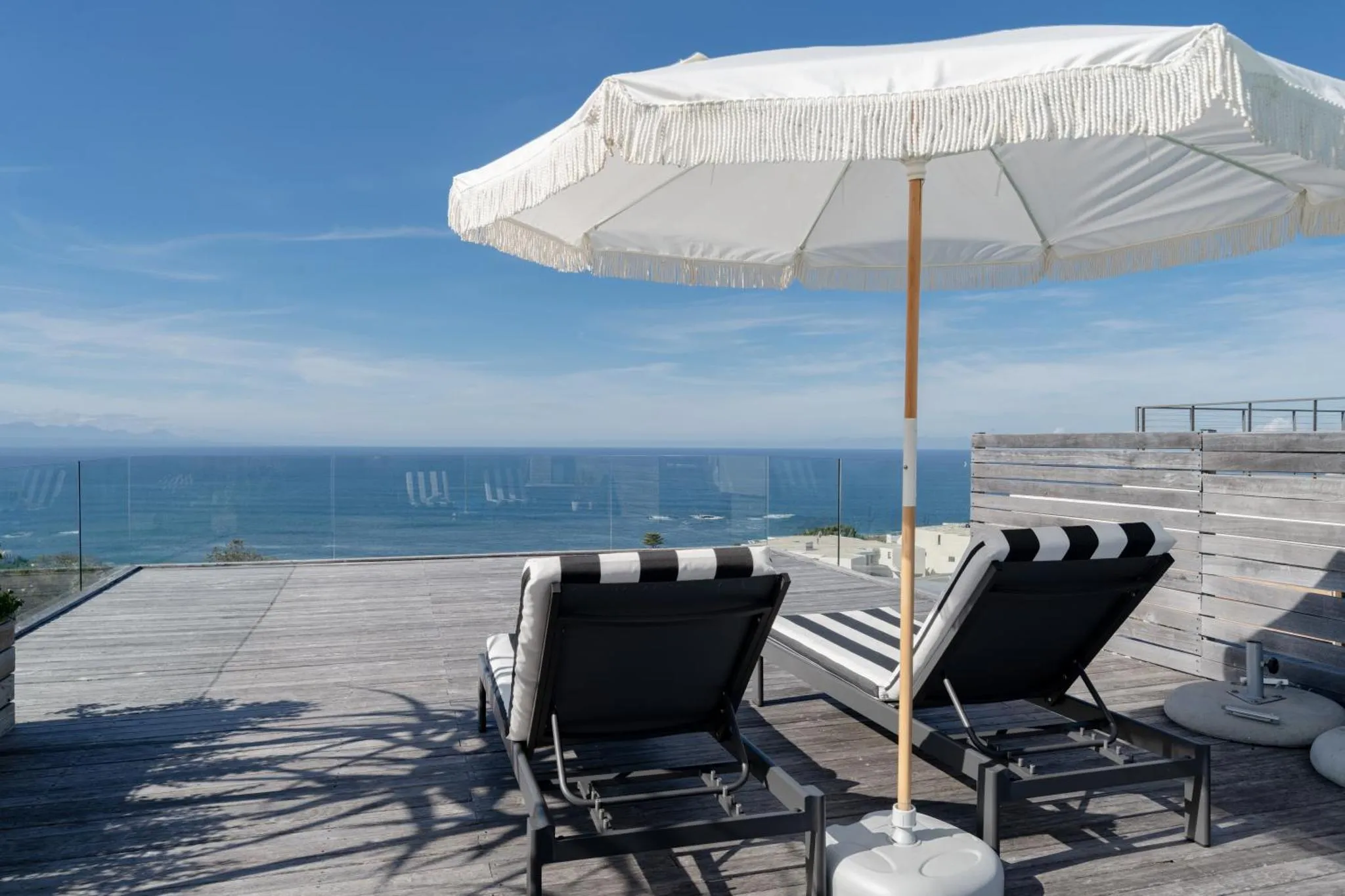 Deux transats rayés se trouvent sur une terrasse en bois avec vue sur la mer.