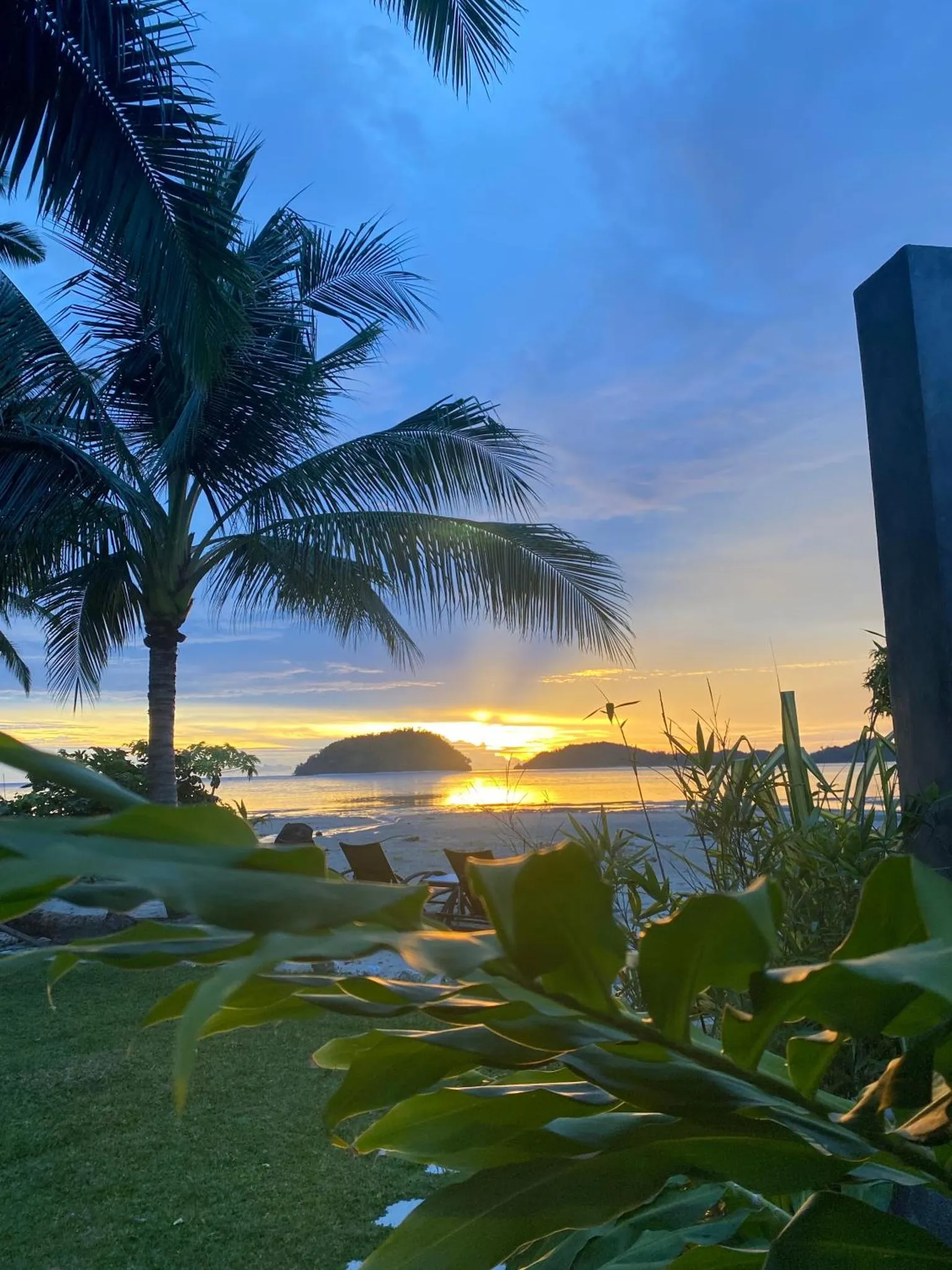 Coucher de soleil sur une plage tropicale avec des palmiers et des transats.