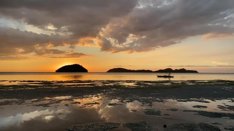 Un coucher de soleil illumine une mer calme avec des îles à l'horizon.