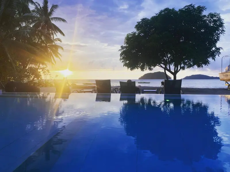 Une piscine bleu clair reflète le ciel au coucher du soleil, avec des transats sur le bord.