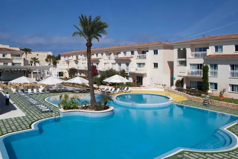 Vue d'une piscine d'hôtel avec des transats et des parasols sous les palmiers.