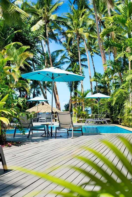 Transats et parasols turquoise bordent une piscine au milieu d'une végétation luxuriante.
