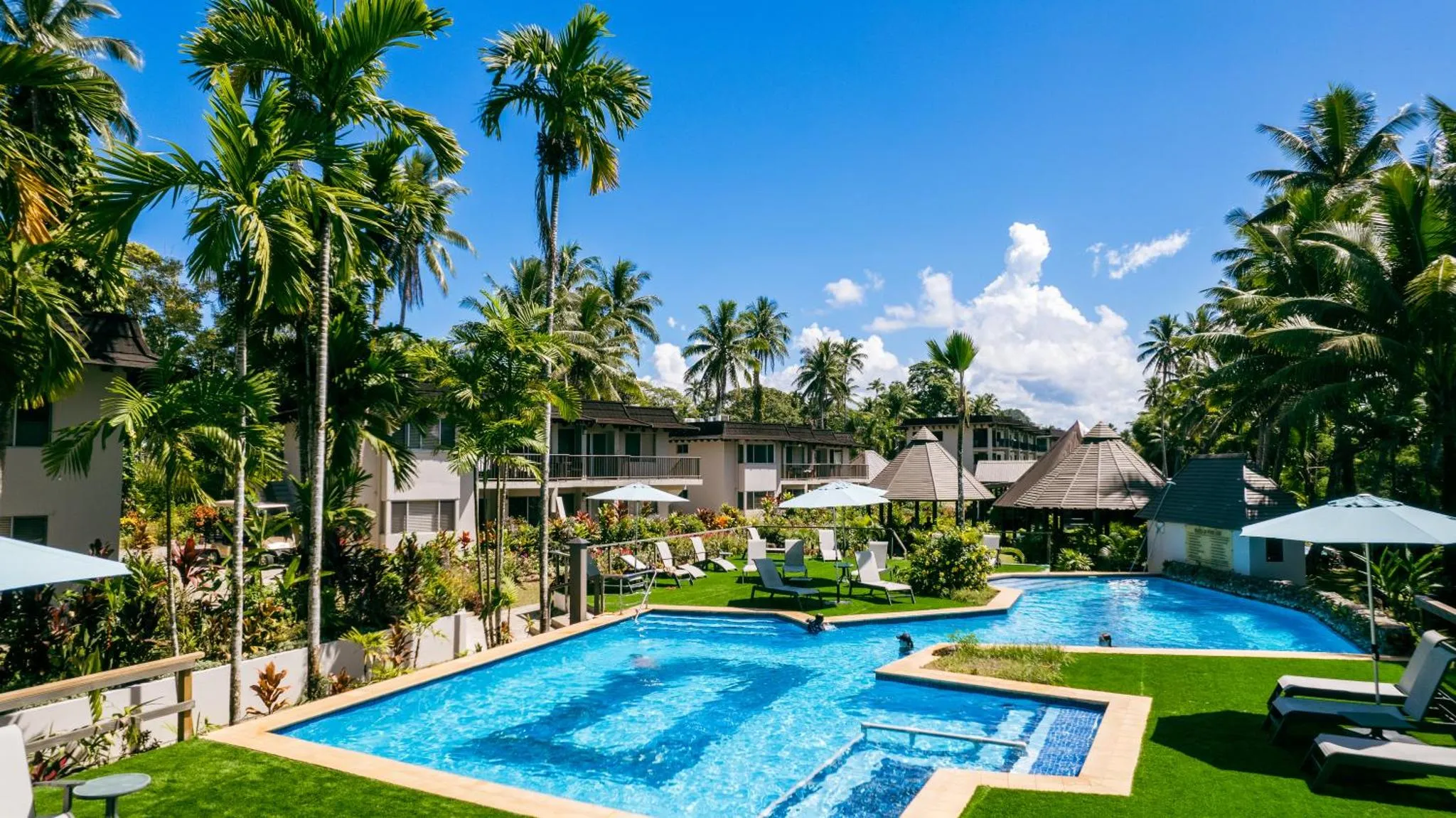 Une piscine bordée de transats et de végétation luxuriante sous un ciel bleu.