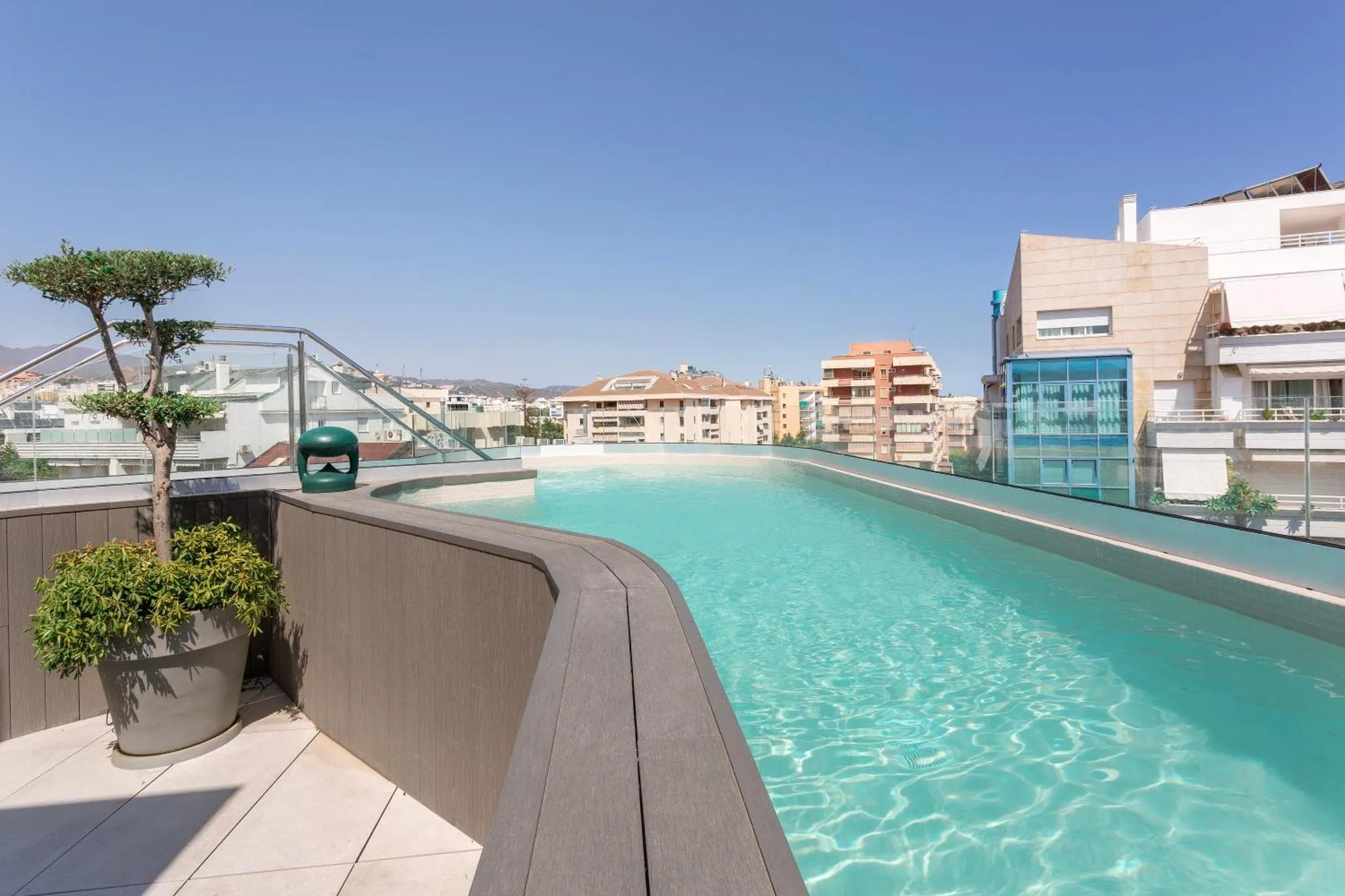 Piscine rectangulaire à débordement sur un toit-terrasse ensoleillé avec vue sur la ville.