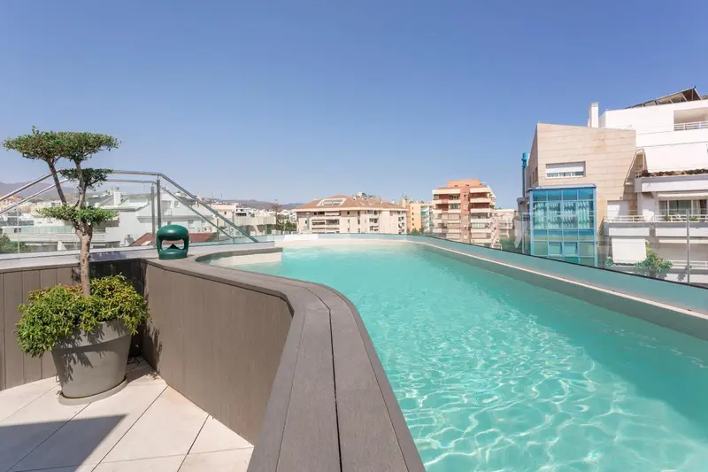 Piscine rectangulaire à débordement sur un toit-terrasse ensoleillé avec vue sur la ville.